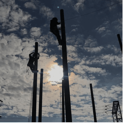 Linemen on poles against sky